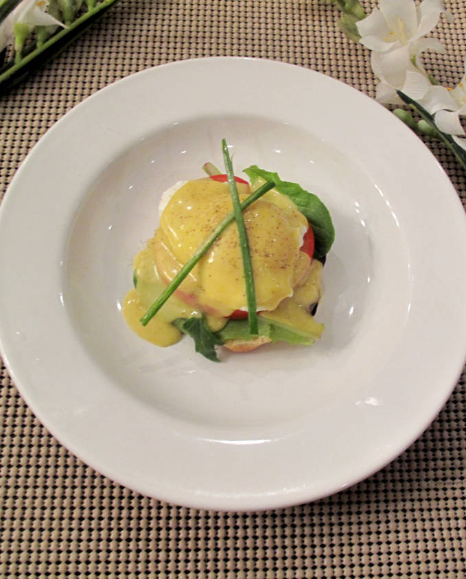 Poached eggs with mixed leafy vegetables, tomato, hollandaise sauce, and homemade english muffins.