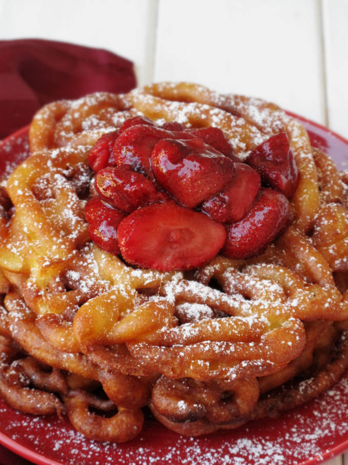 A close up shot of fresh funnel cake with strawberries and icing sugar. Want a closer shot? Say.. right next to your face? Click to get the amazing and simple recipe!