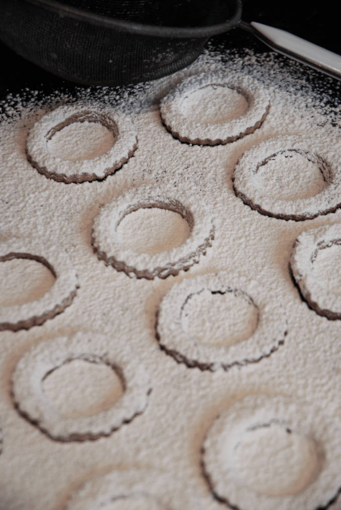 Dusting pecan linzer cookies with icing sugar. Click for the recipe!