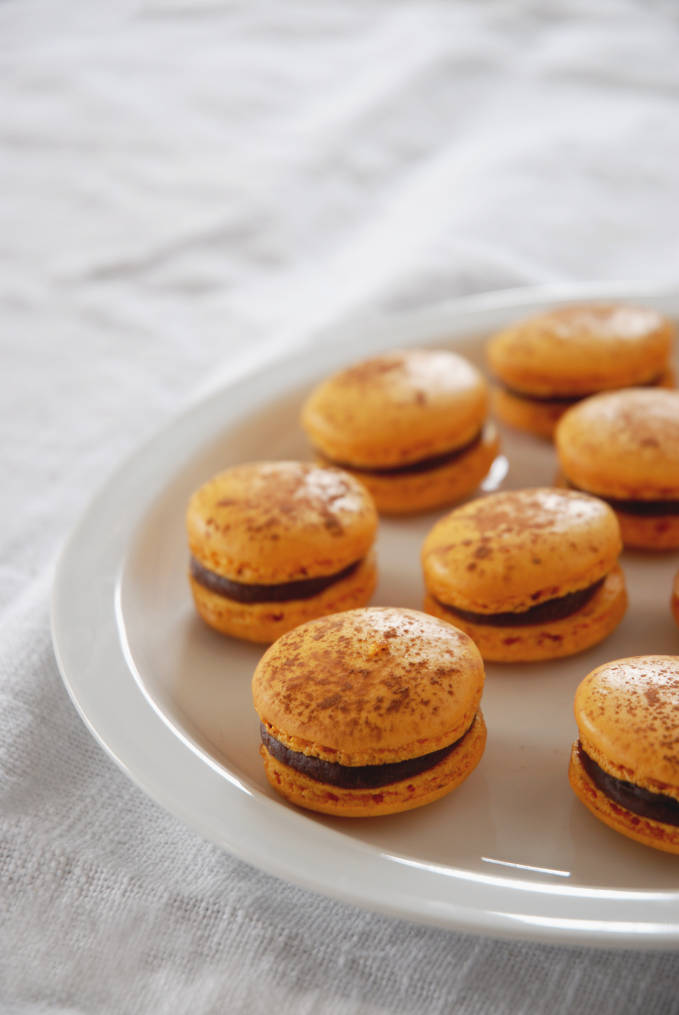 Passion fruit & milk chocolate French macarons on a plate... but wouldn't they be better in your mouth? Click to get the recipe!