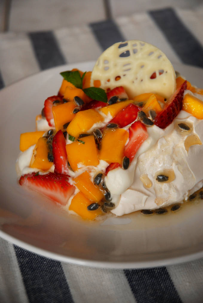 Mango, strawberry, and passion fruit pavlova with a mint syrup and white chocolate decoration. Don't you just want to take a bite? Stop dreaming! Click to get the recipe.
