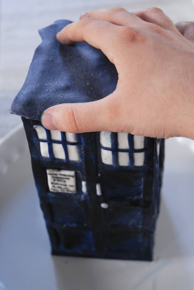 Attaching TARDIS modelling chocolate roof to cake--click to see the full photo tutorial so YOU CAN MAKE YOUR OWN DOCTOR WHO TARDIS CAKE! #diy