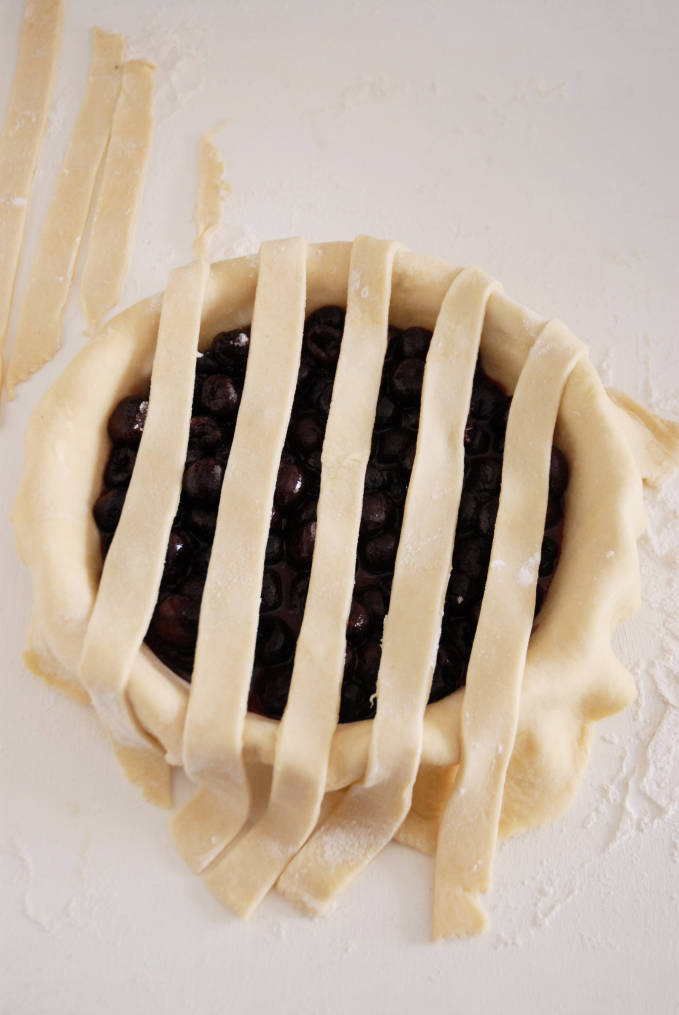 Adding strips of pie dough to a pie to make a lattice crust--click to get a step-by-step photo tutorial on lattice pie crusts, so you can make them easily!