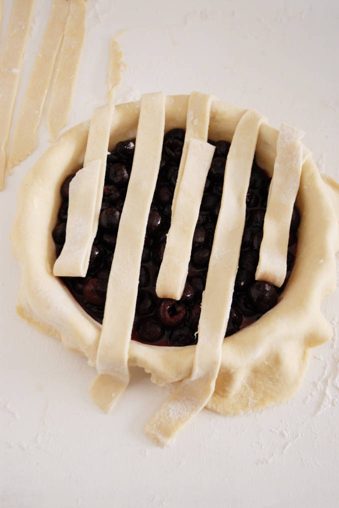 Adding strips of pie dough to a pie to make a lattice crust--click to get a step-by-step photo tutorial on lattice pie crusts, so you can make them easily!