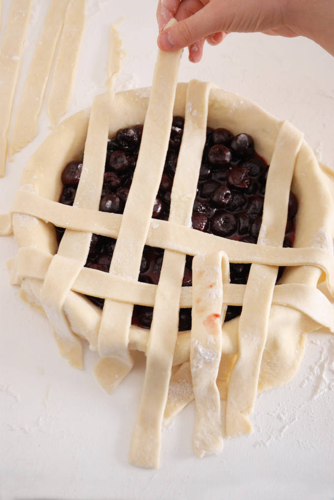 Adding strips of pie dough to a pie to make a lattice crust--click to get a step-by-step photo tutorial on lattice pie crusts, so you can make them easily!