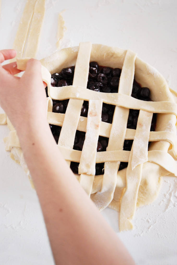 Adding strips of pie dough to a pie to make a lattice crust--click to get a step-by-step photo tutorial on lattice pie crusts, so you can make them easily!