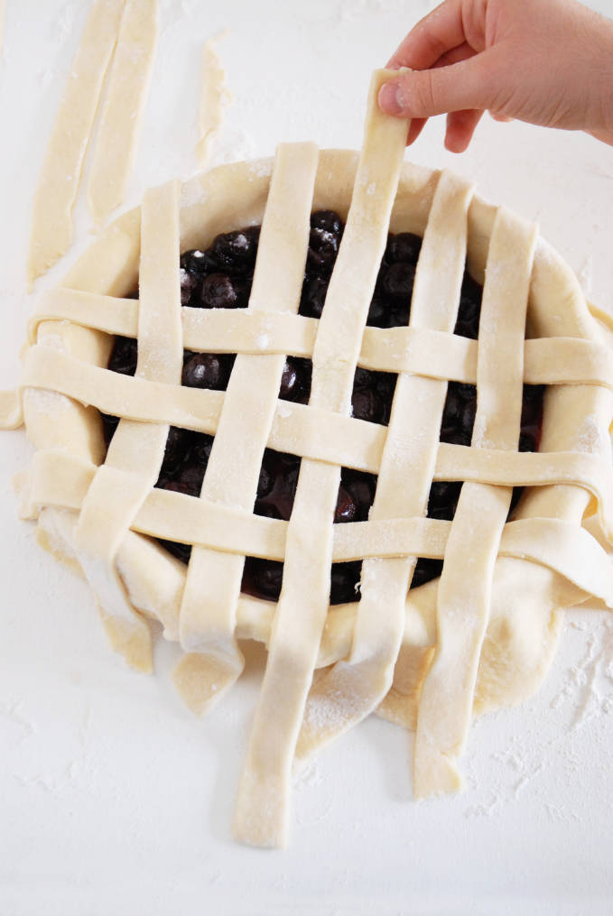 Adding strips of pie dough to a pie to make a lattice crust--click to get a step-by-step photo tutorial on lattice pie crusts, so you can make them easily!